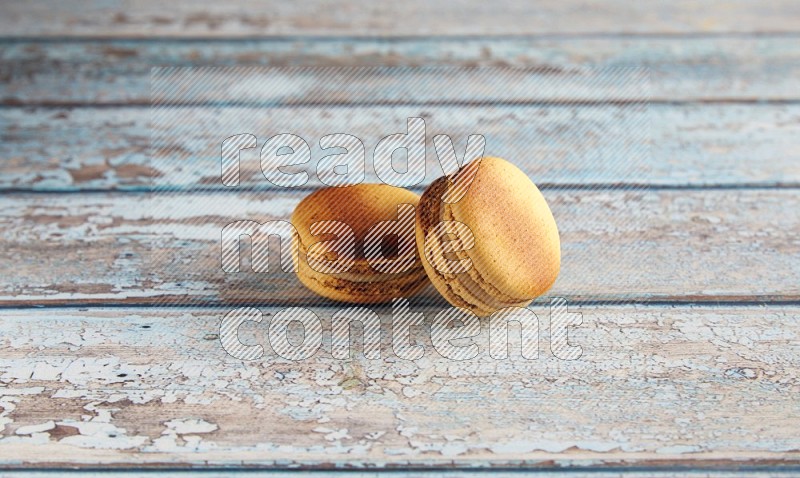 45º Shot of two Yellow Crème Brulée macarons on light blue wooden background