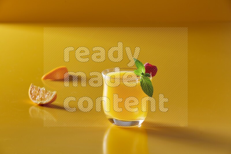 glass of orange juice with berry & mint on yellow background