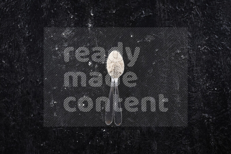 ملعقتان معدنيتان أحدهما ممتلئة ببودرة البصل علي خلفية سوداء