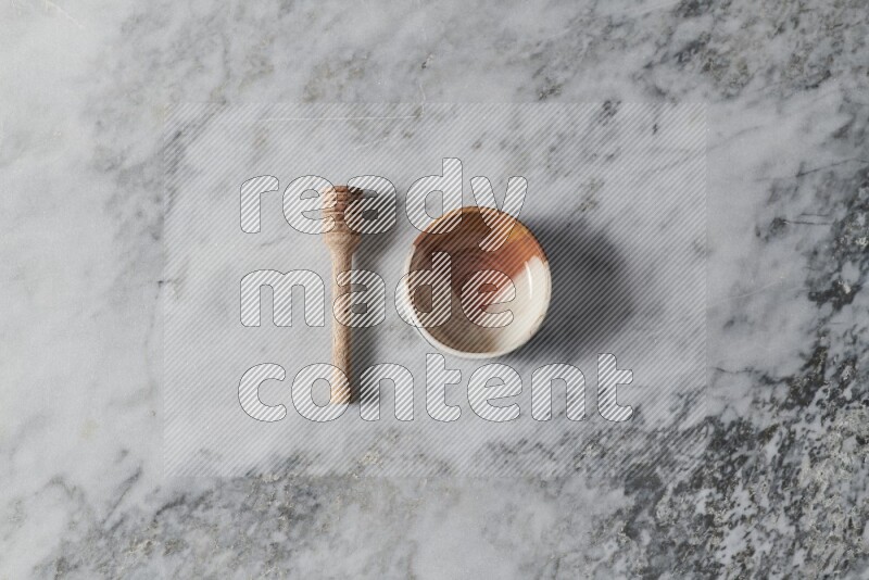 Multicolored pottery bowl with wooden honey dipper on the side on grey marble background