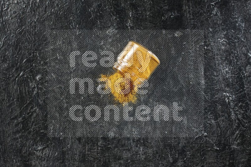 وعاء زجاجي مقلوب ممتلئ ببودرة الكركم والبودرة تناثرت منه على خلفية سوداء