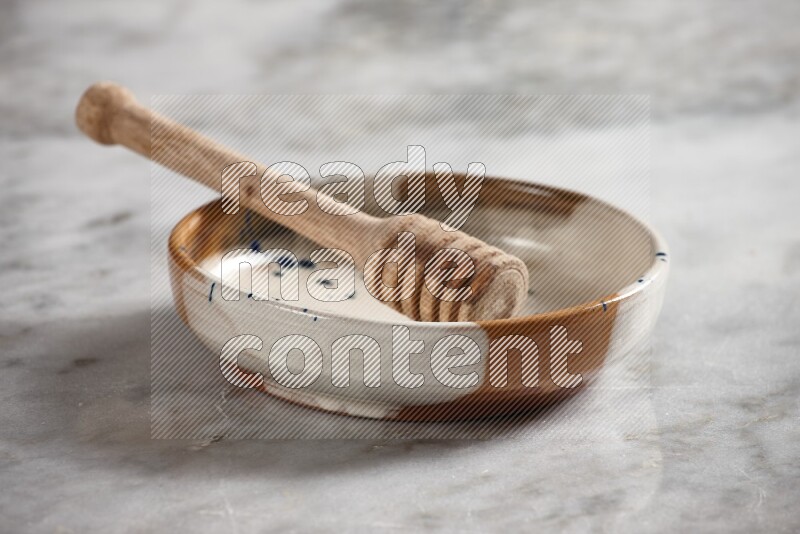 Multicolored pottery bowl with wooden honey dipper in it on grey marble background