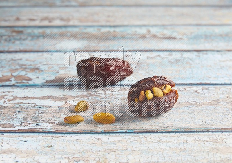 two pistachio stuffed madjoul dates on a light blue wooden background