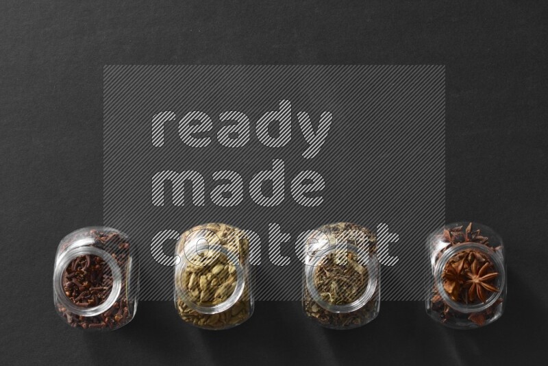 قرنفل وحبوب الهيل وريحان مجفف ويانسون نجمي في أوعية زجاجية علي خلفية سوداء