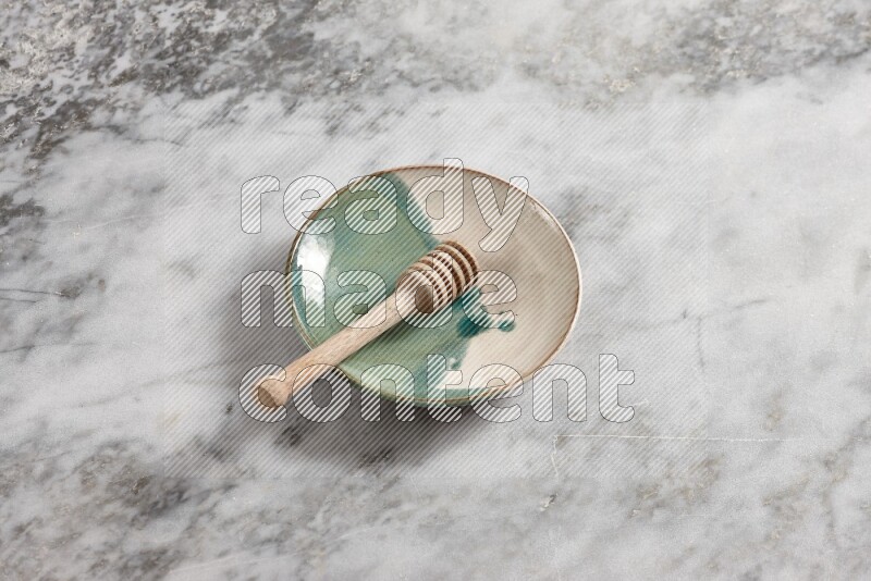 Multicolored pottery plate with wooden honey dipper in it on grey marble background