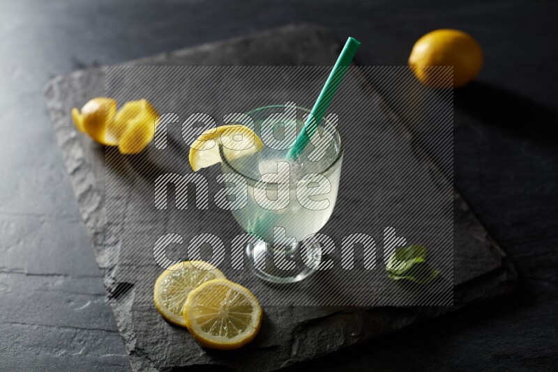 A glass of lemon juice with a straw on black background