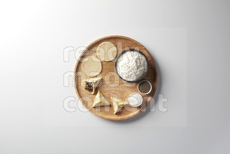 two closed sambosas and one open sambosa filled with meat while flour, salt, and black pepper aside in a wooden dish on a white background