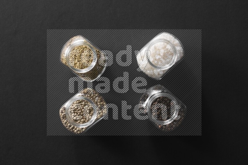 ملح وفلفل أسود وفلفل أبيض وكمون في أوعية زجاجية علي خلفية سوداء