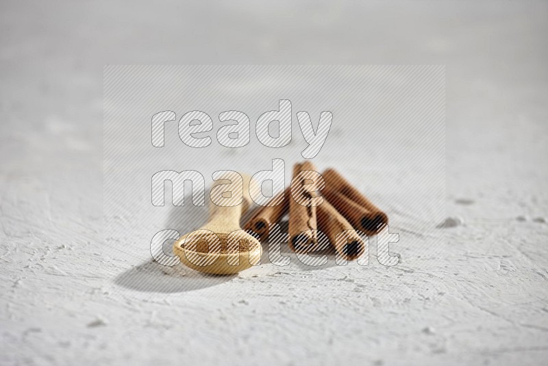 Cinnamon powder in a wooden spoon with cinnamon sticks on white background