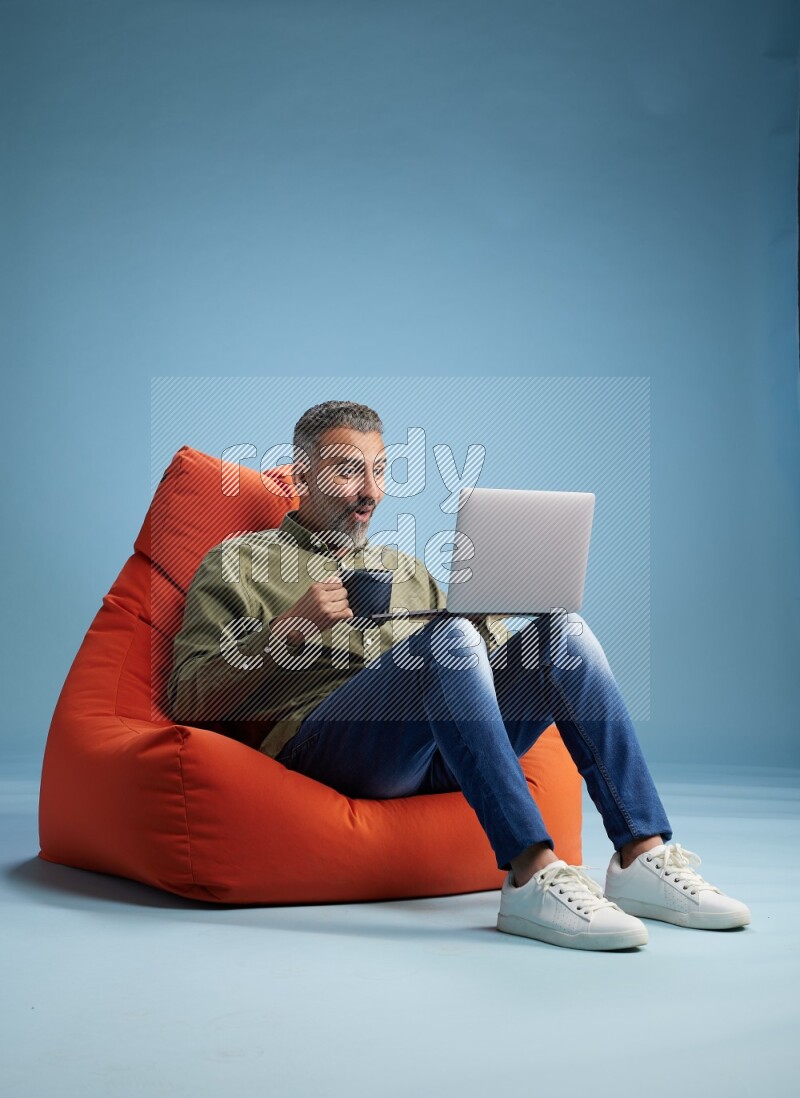 A man sitting on an orange beanbag and working on laptop