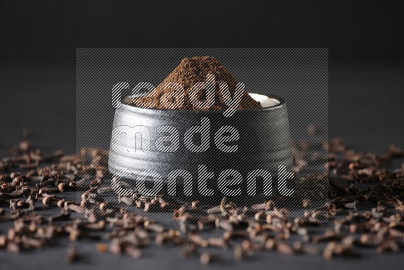 وعاء فخاري أسود ممتلئ ببودرة القرنفل وحبوب القرنفل على خلفية سوداء