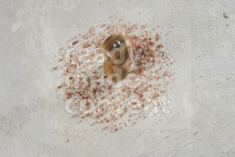 A wooden grinder standing upright and surrounded by coarse pink himalayan salt on white background