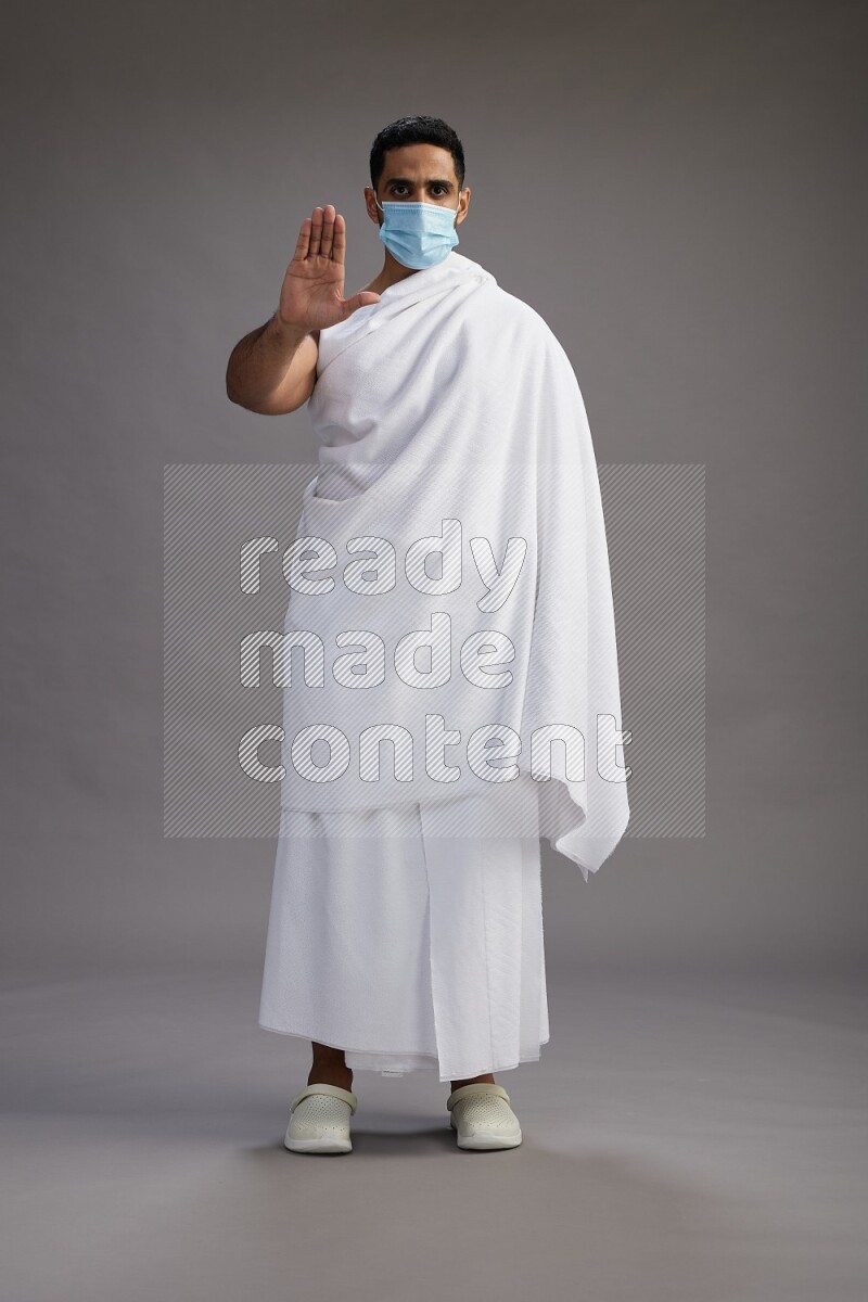 A man wearing Ehram with face mask Standing Interacting with the camera on gray background