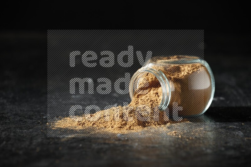 وعاء زجاجي للتوابل مقلوب ممتلئ ببودرة بهار الفلفل الحلو والبودرة تناثرت منه على خلفية سوداء