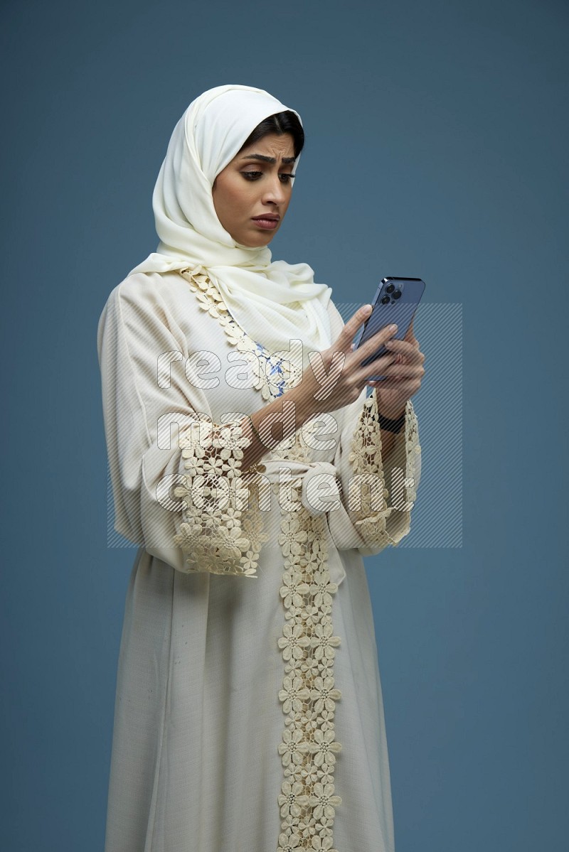 A Saudi woman Texting in a blue background wearing an off-white Abaya Hijab