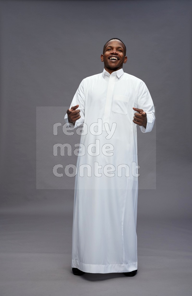 Saudi man wearing thob standing interacting with the camera on gray background