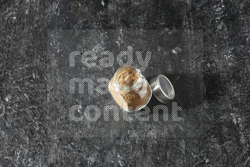 وعاء زجاجي للتوابل ممتلئ ببودرة بهار الفلفل الحلو على خلفية سوداء