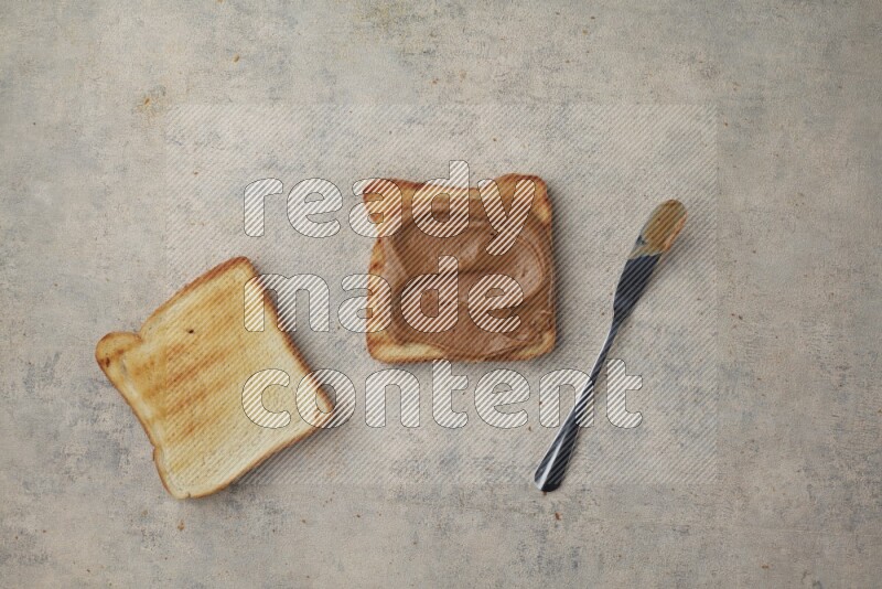 Creamy peanut butter on a toasted white toast and toasted white toast slices on a light blue textured background