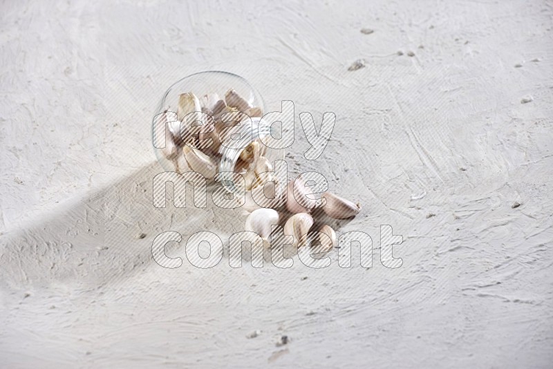 A glass spice jar full of garlic cloves flipped and the cloves came out on a textured white flooring in different angles