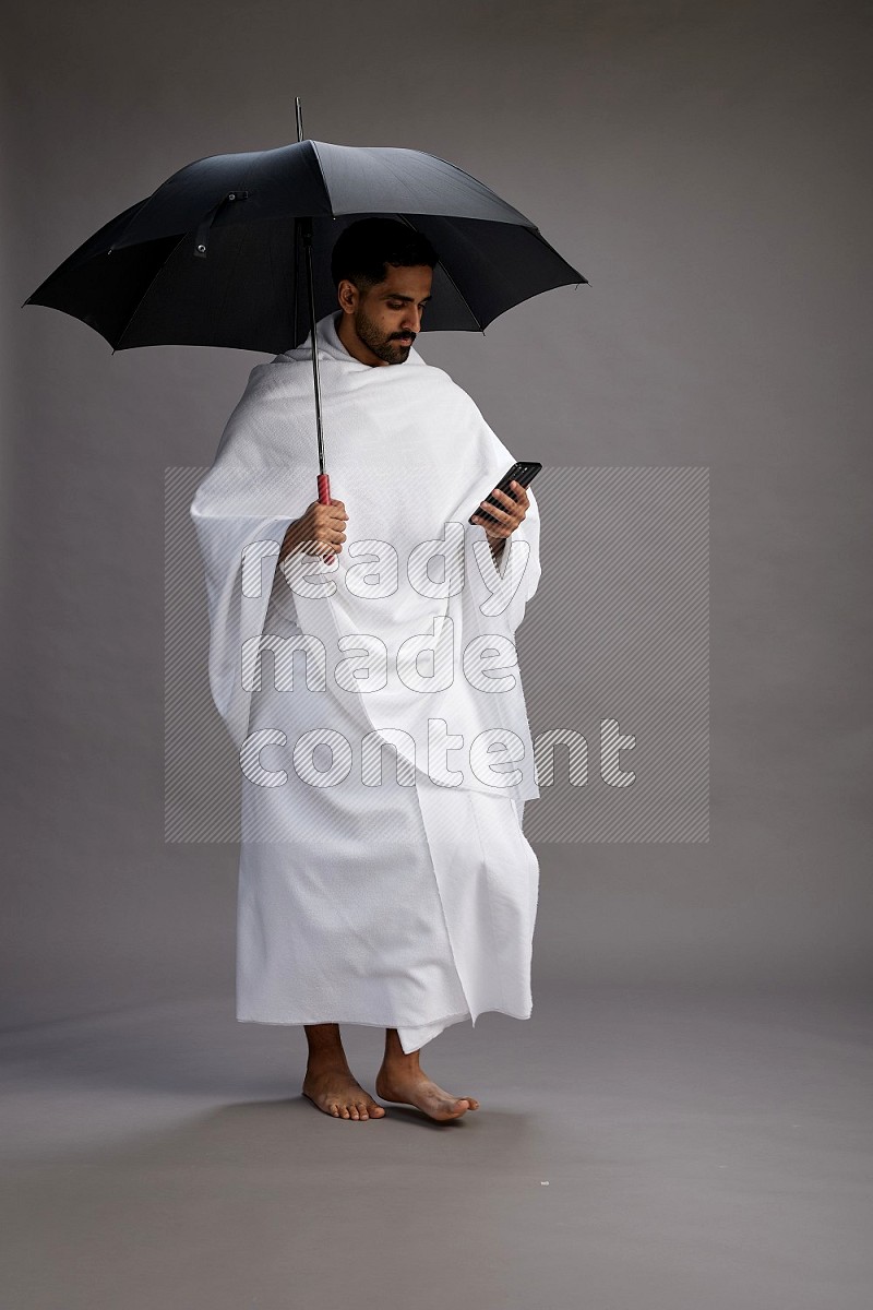 A man wearing Ehram Standing holding umbrella on gray background