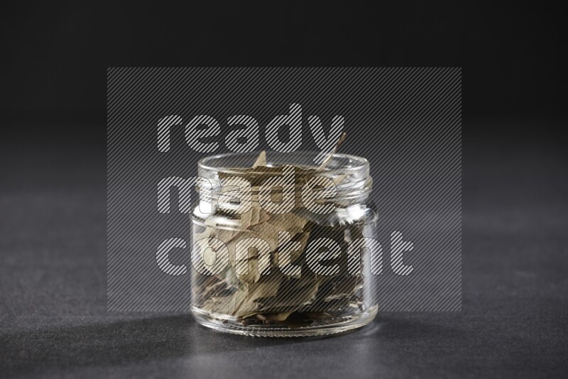 A glass jar filled with dried bay leaves on black flooring