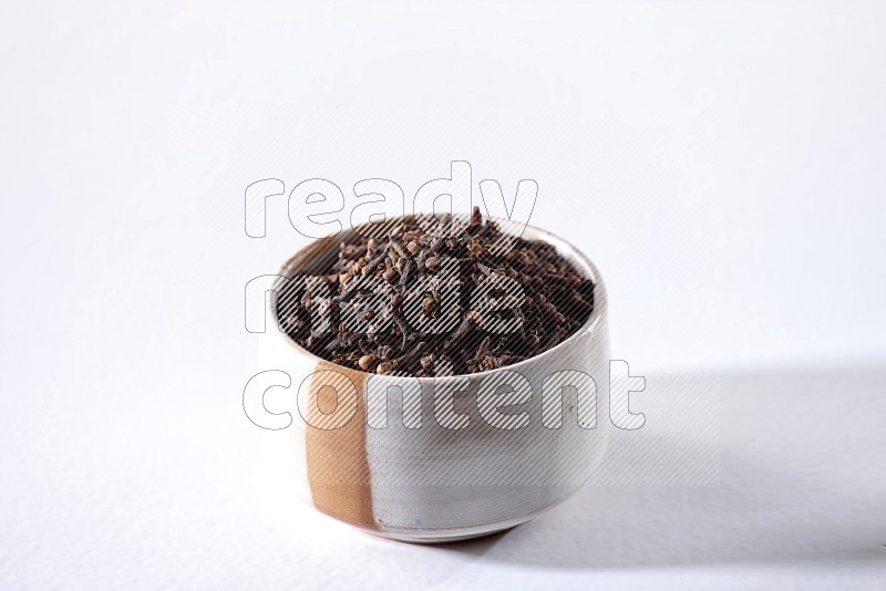 A beige ceramic bowl full of cloves on a white flooring