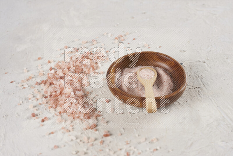 A pottery plate full of fine salt with bunch of coarse salt beside it on white background