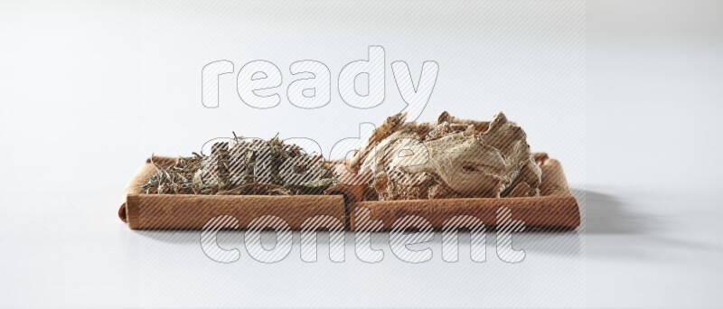 مربعان من أعواد القرفة ممتلئان بالزنجبيل المجفف والريحان المجفف علي خلفية بيضاء