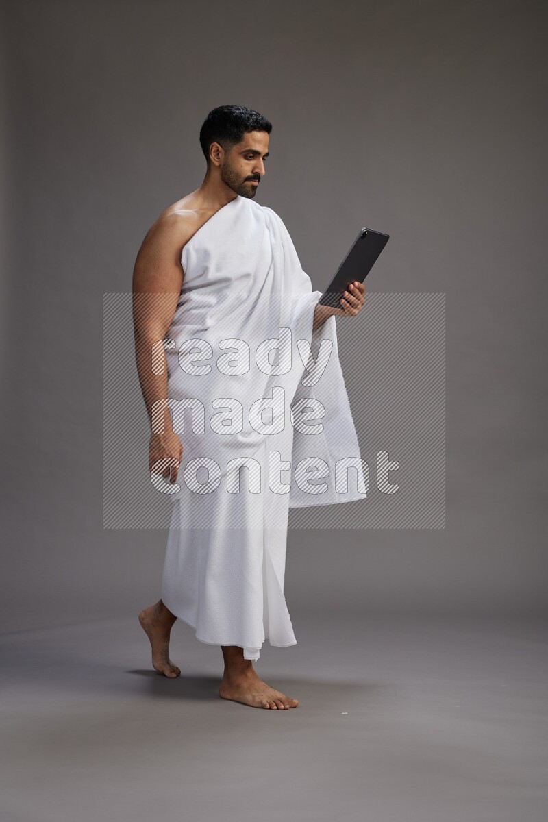 A man wearing Ehram and holding a tablet on gray background