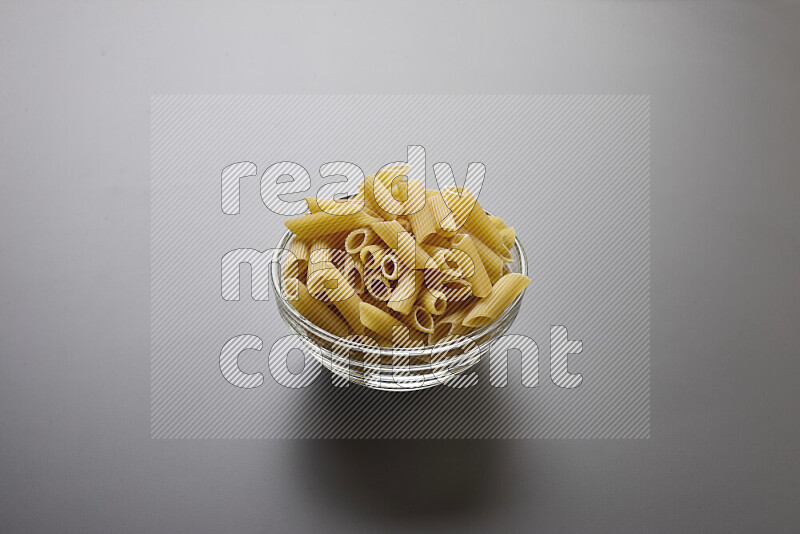 Penne pasta in a glass bowl on grey background