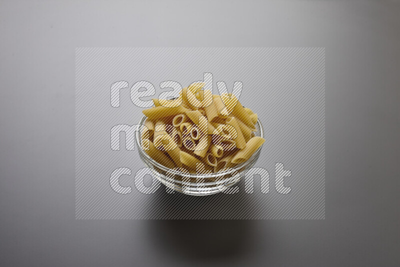 Penne pasta in a glass bowl on grey background