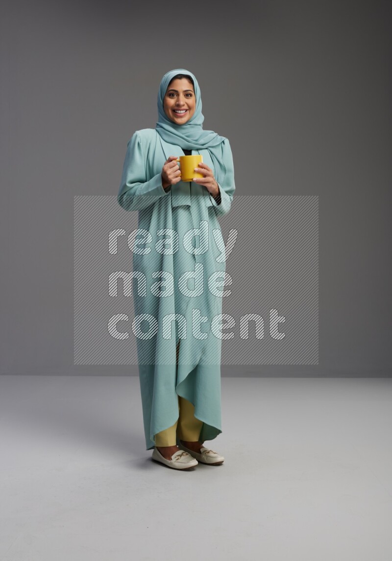 Saudi Woman wearing Abaya standing  holding a mug on Gray background