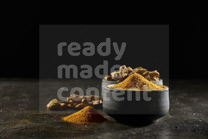 وعاءان من الفخار باللون الأسود، أحدهما ممتلئ ببودرة الكركم والآخر ممتلئ بأصابع كاملة من الكركم المجفف على خلفية سوداء