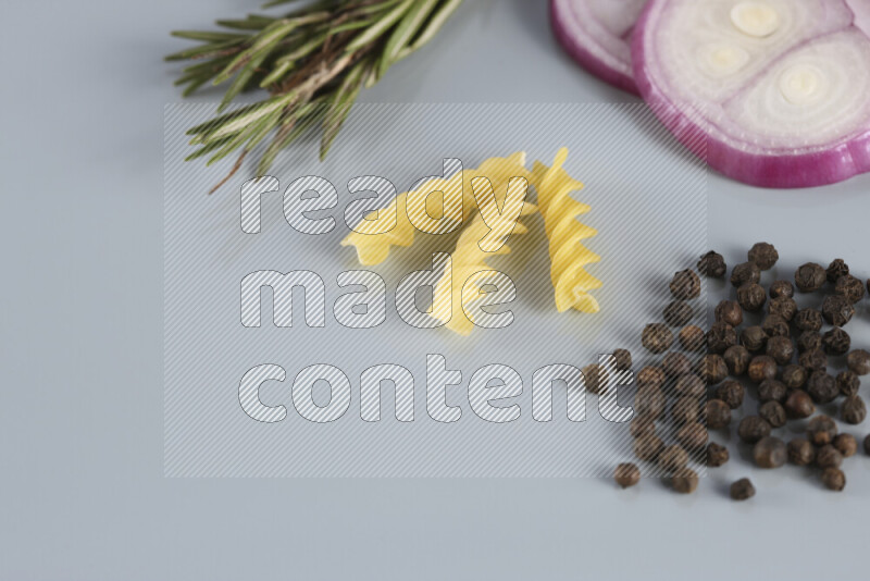 Raw pasta with different ingredients such as cherry tomatoes, garlic, onions, red chilis, black pepper, white pepper, bay laurel leaves, rosemary, cardamom and mushrooms on light blue background