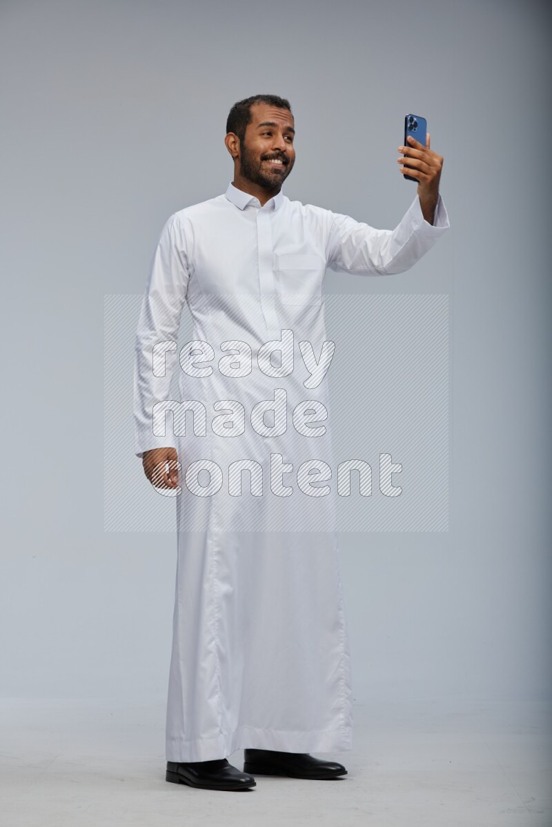 Saudi man wearing Thob standing taking selfie on Gray background
