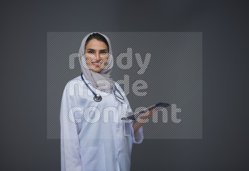 A Saudi doctor wearing a light gray head scarf standing and crossing her hands eye level on a grey background