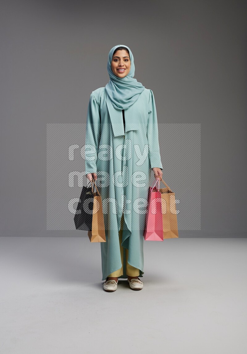 Saudi Woman wearing Abaya standing holding shopping bag on Gray background