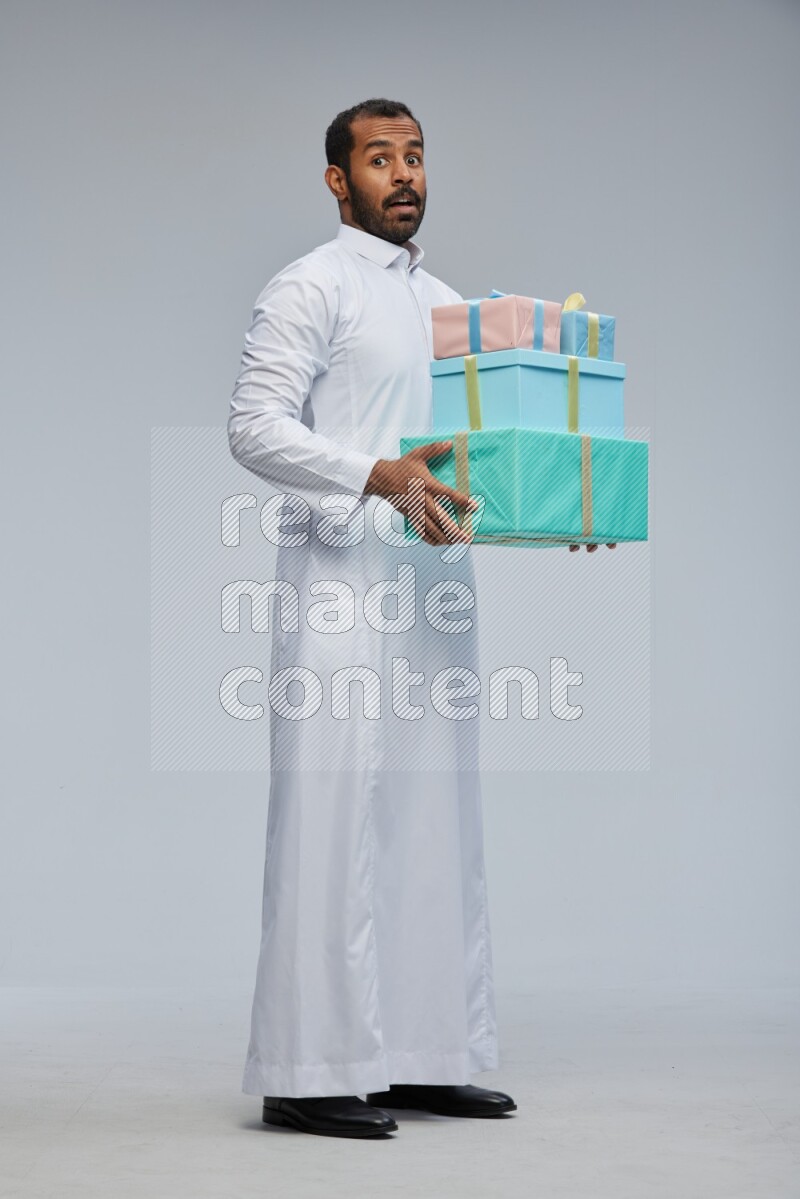 Saudi man Wearing thob standing holding gift box on Gray background