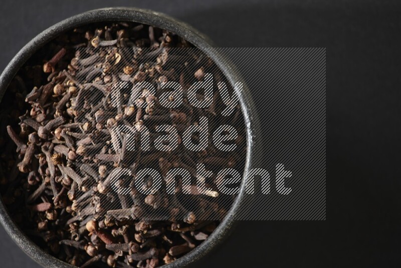 وعاء فخاري أسود ممتلئ بحبوب القرنفل علي خلفية سوداء