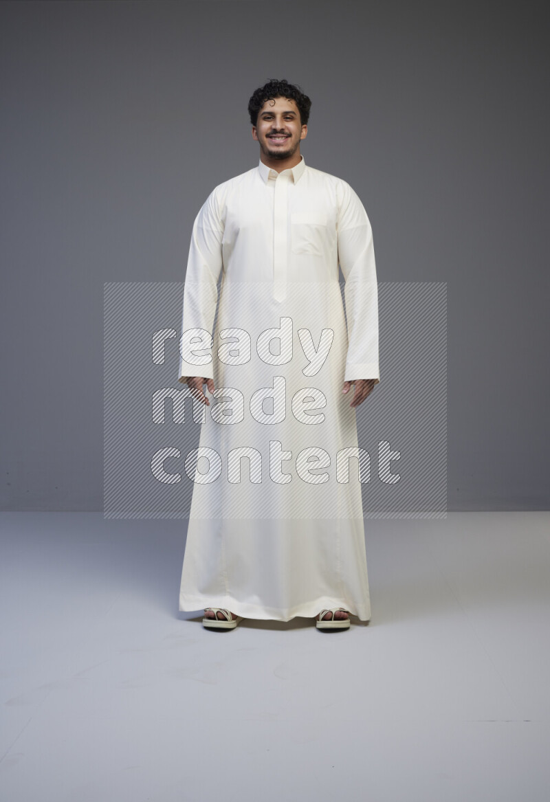 A Saudi man standing wearing thob interacting with the camera on gray background