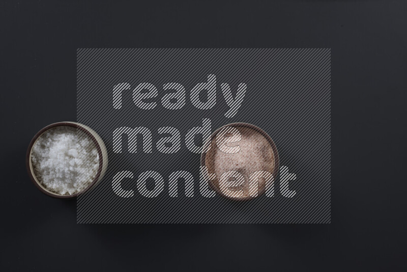 2 وعاء فخاري احدهمها ممتلئ بملح الهيمالايا والأخر بالملح الأبيض على خلفية سوداء