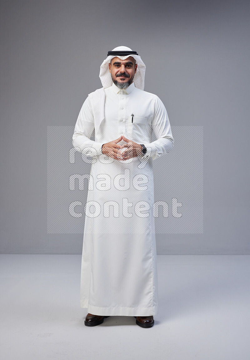 Saudi man Wearing Thob and white Shomag standing interacting with the camera on Gray background