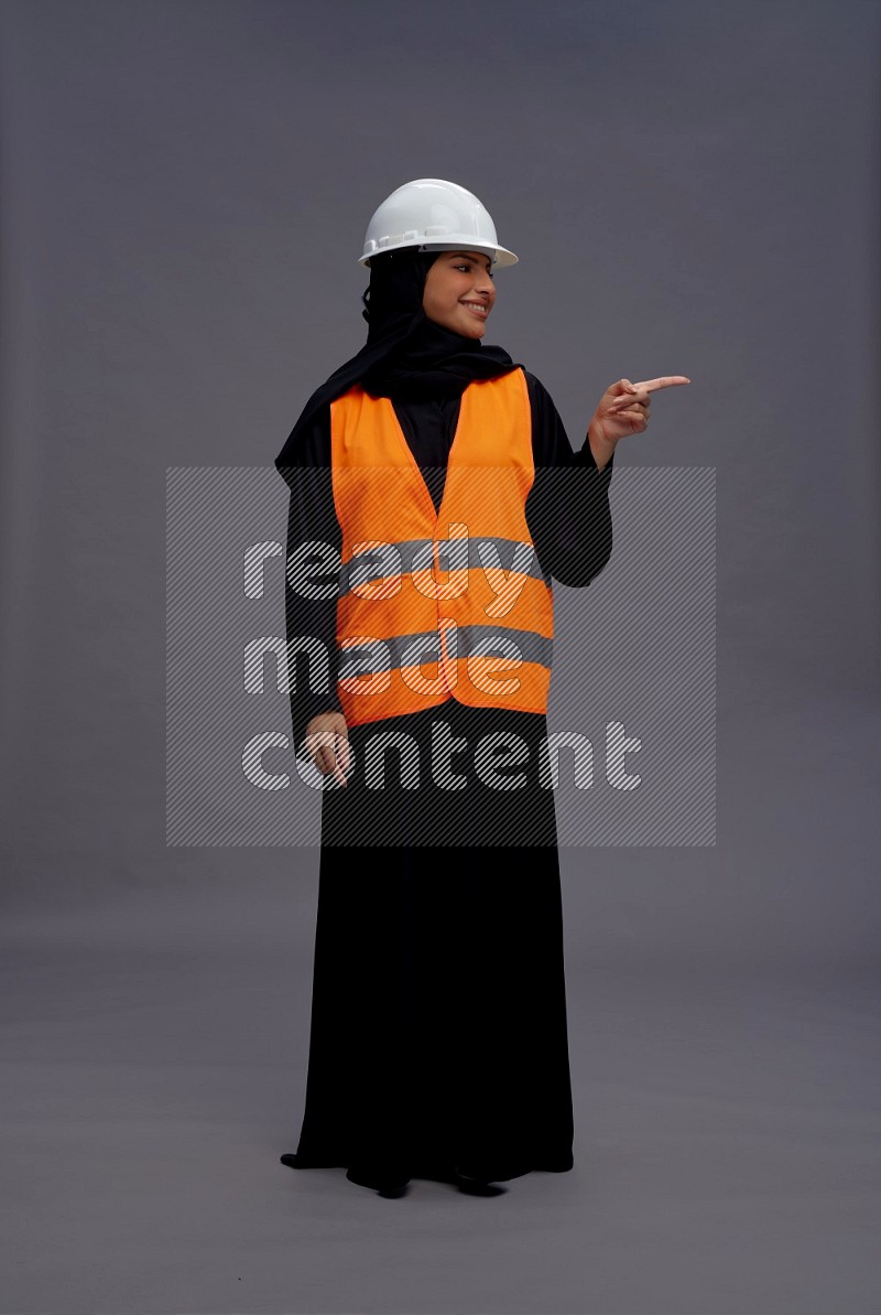 Saudi woman wearing Abaya with engineer vest standing interacting with the camera on gray background