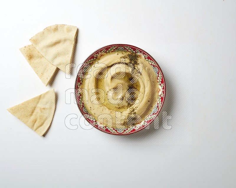 Hummus in a red plate with patterns garnished with zaatar & sumak on a white background