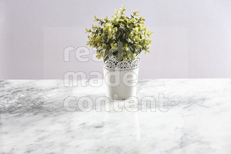 Green artificial plant in white decorative pot on grey marble background