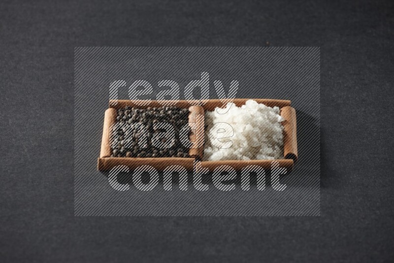 مربعان من أعواد القرفة ممتلئان بالملح الأبيض وحبوب الفلفل الأسود علي خلفية سوداء