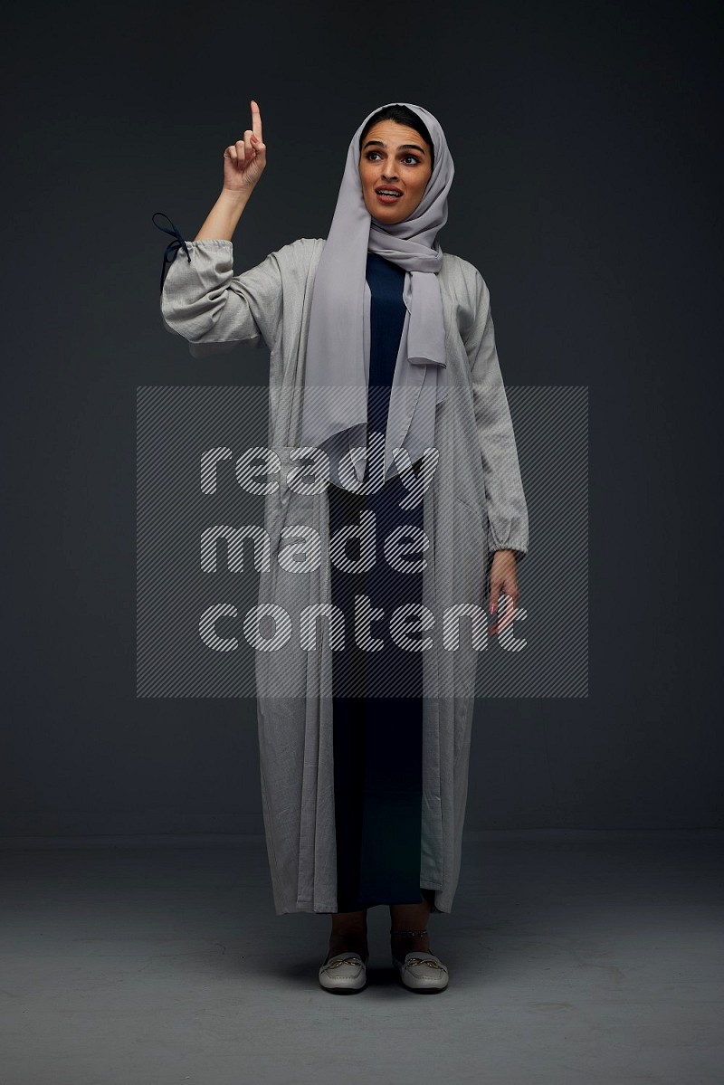 A Saudi woman wearing a light gray Abaya and head scarf standing and making multi poses eye level on a grey background