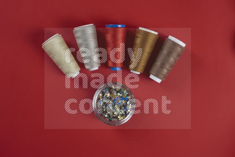 A brown and red collection of sewing and tailoring tools arranged on a red background