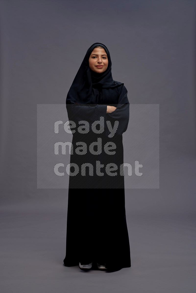 Saudi woman wearing Abaya standing with crossed arms on gray background