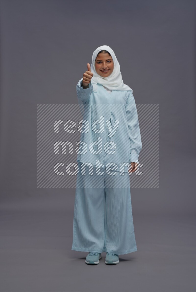 Saudi woman wearing hijab clothes standing interacting with the camera on gray background